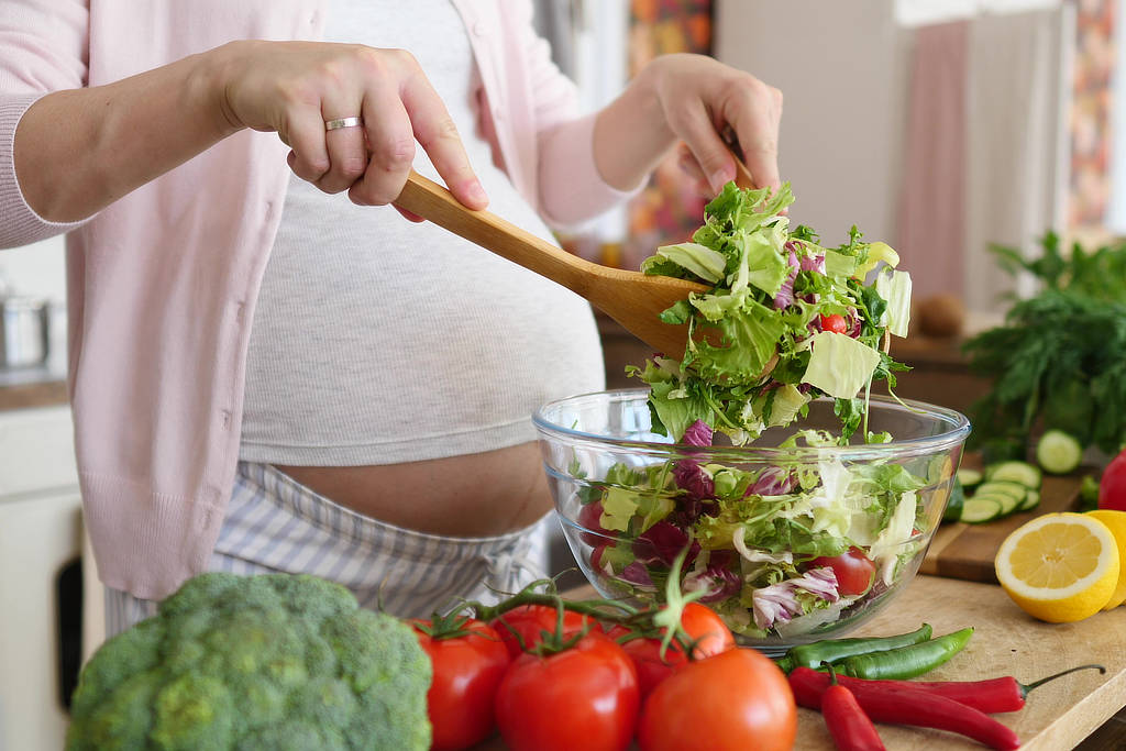 Schwangere Frau in der Küche, die einen gesunden Salat zubereitet